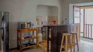A compact kitchen with a refrigerator, microwave, and a wooden bar stool. - CENTRAL PLAZA APARTMENTS (Cusco)