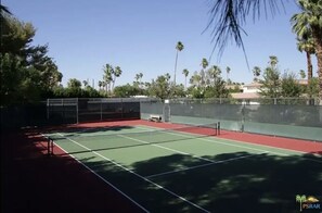 Ein Tennisplatz mit Netz, umgeben von einem Zaun und Palmen.