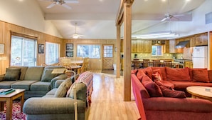 A spacious living room with a wooden floor, a red sofa, a grey sofa, and a dining area with wooden furniture. - Yosemite's Riverfront Retreat (Yosemite National Park)