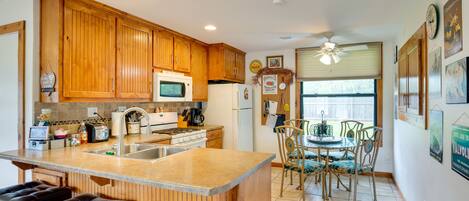 A kitchen with wooden cabinets, a microwave, a refrigerator, and a dining area with chairs and a table.