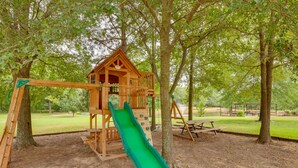 Une structure de jeux en bois avec un toboggan, entourée d’arbres.