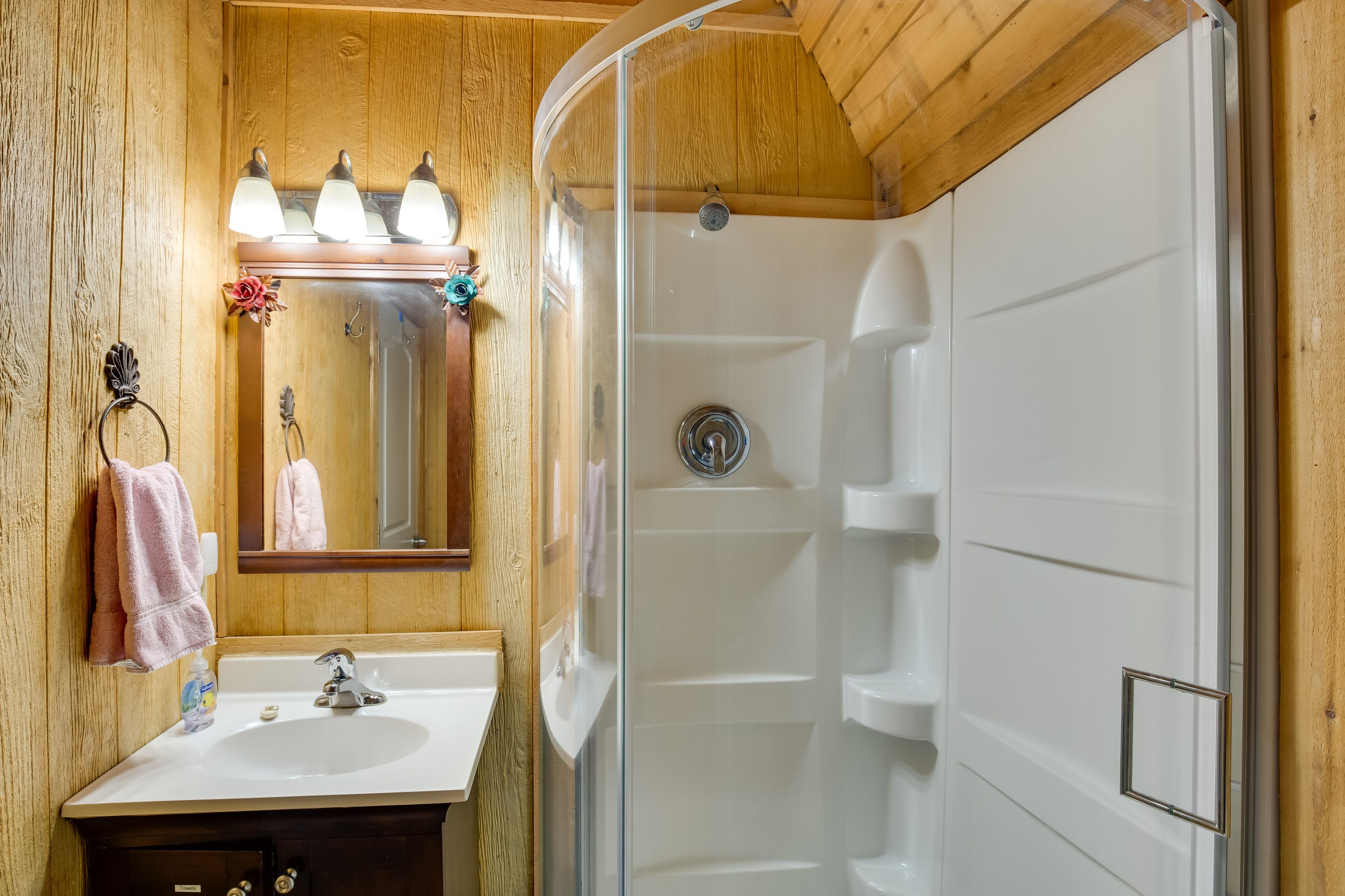 Ein Badezimmer einer Holzhütte mit Waschbecken, Spiegel und Dusche.