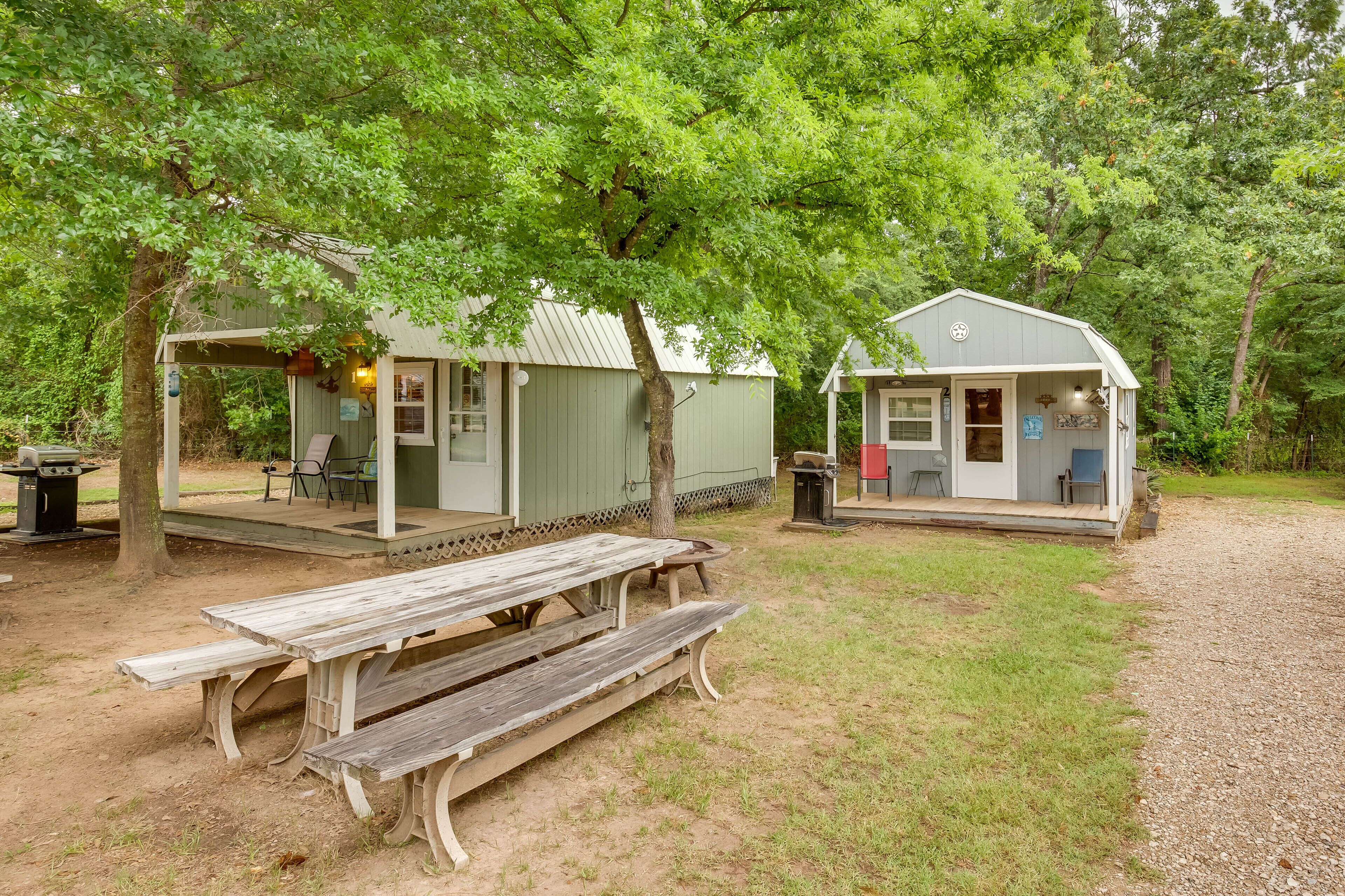 A rustic cabin with a porch and a picnic table in a wooded area.