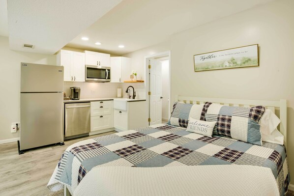 A bedroom with a large bed, a bedside table, and a nightstand. There is a window with curtains, a wall-mounted TV, and a framed picture on the wall. - Cozy Studio Stay in Liberty: Hike, Relax, Explore! (Liberty)