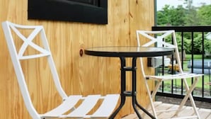 En træterrasse med to hvide metalstole og et lille rundt bord.