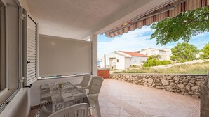 Eine überdachte Terrasse mit Tisch und Stühlen, einer Steinmauer und Blick auf Häuser und Grünflächen.