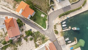Ein Luftbild einer Küstenwohngegend mit Häusern, einer Straße und Booten, die an einem Steg liegen.