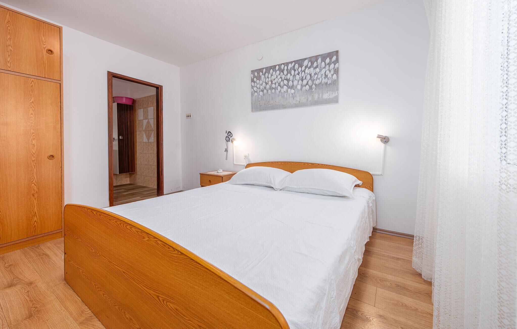 A bedroom with a wooden bed, a nightstand, a wall-mounted lamp, and a door leading to another room.