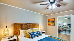 Quarto com cabeceira de madeira, cama com manta listrada colorida, duas mesas de cabeceira com luminárias e um ventilador de teto.