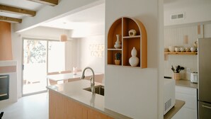 Una cucina moderna con isola centrale, travi in legno ed elementi a giorno contenenti oggetti decorativi.