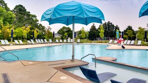 Ein Swimmingpool mit blauen Sonnenschirmen, Liegestühlen und einer gefliesten Liegefläche.