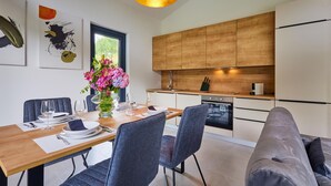 A modern kitchen with wooden cabinets, a dining area with a wooden table and chairs, and a vase of flowers on the table.