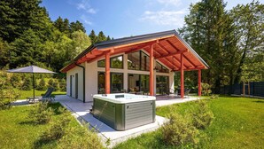 A modern house with a covered patio, a hot tub, and a lawn.