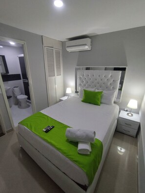 A neatly arranged bedroom with a large bed, a bedside table, a nightstand, an air conditioning unit, and a bathroom visible through an open door. - Hotel BM-17  Cerca Al Mar  (Cartagena)