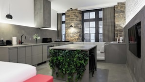 A modern kitchen with a stone accent wall, a built-in island with greenery, and a large window with curtains.