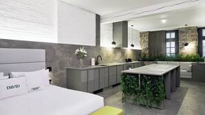 A modern hotel room with a bed, a small island with plants, a kitchenette, and a large window. - PREMIUM LOFT | The Signature (Montréal)