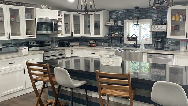 Una cucina moderna con mobili bianchi, un'isola centrale con sgabelli da bar, forno integrato e macchina per il caffè.