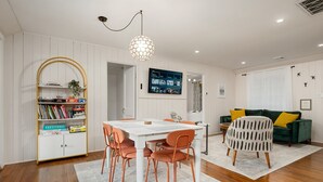 A modern living room with a dining area, white walls, wooden flooring, a bookshelf, a TV, and a green sofa with yellow cushions. - Seneca Lake Waterfront Cottage with Hot Tub on FLX Wine Trail (Burdett)