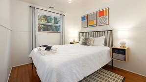 A neatly made bed with a white duvet, a bedside lamp, and a small wooden nightstand with a lamp. - Seneca Lake Waterfront Cottage with Hot Tub on FLX Wine Trail (Burdett)