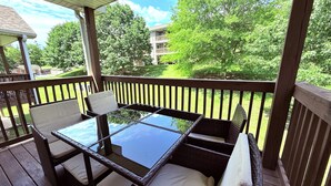 Un espace extérieur aménagé, abrité et doté d’une table en verre et de chaises en osier, entouré d’une terrasse en bois et offrant une vue sur un paysage verdoyant.