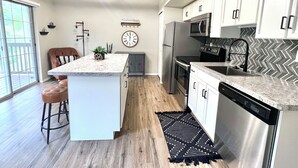 Une cuisine moderne dotée d’un îlot central, d’appareils électroménagers en acier inoxydable et d’un dosseret en carreaux disposés en motif chevrons.