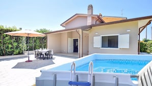 Et hus med swimmingpool, udendørs møbler og en overdækket terrasse.