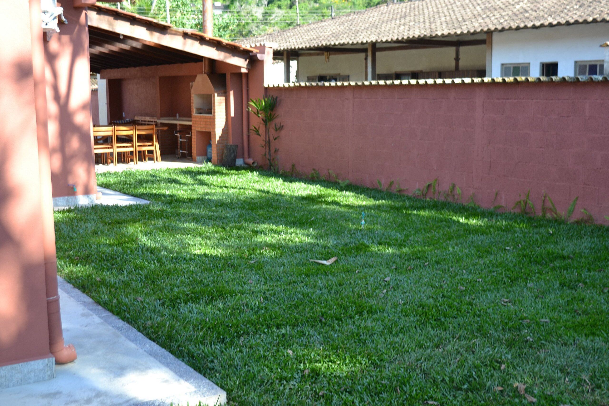 A backyard with a patio, a covered seating area, and a house with a tiled roof.