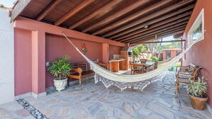 A covered patio with a hammock, stone flooring, wooden furniture, and potted plants. - 4 quartos piscina 350 m praia (São Sebastião)