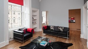Una sala de estar moderna con un sofá negro, una mesa de centro de vidrio y una pared decorada en rojo.