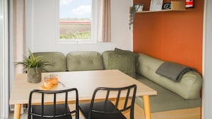 A cozy room with a wooden table, two black chairs, a green sofa, a window with curtains, and a shelf with a clock and a plant. - Gorgeous apartment in Schoonloo (Schoonloo)