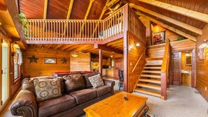 Ein gemütliches Blockhaus-Interieur mit einer Holztreppe, einem Ledersofa und einem Billardtisch.