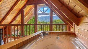 Ein Whirlpool in einer Holzhütte mit einem Balkon mit Blick auf eine gebirgige Landschaft.