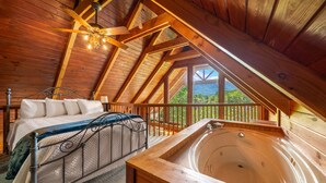 Ein Schlafzimmer mit einem Bett, Holzbalkendecke und Blick ins Freie.