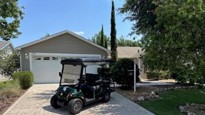 A golf cart parked on a paved driveway in front of a house with a garage. - Beautiful 3 bed / 2 bath home near Lake Sumter w/ cart, 2 bikes and wi-fi!   (The Villages)