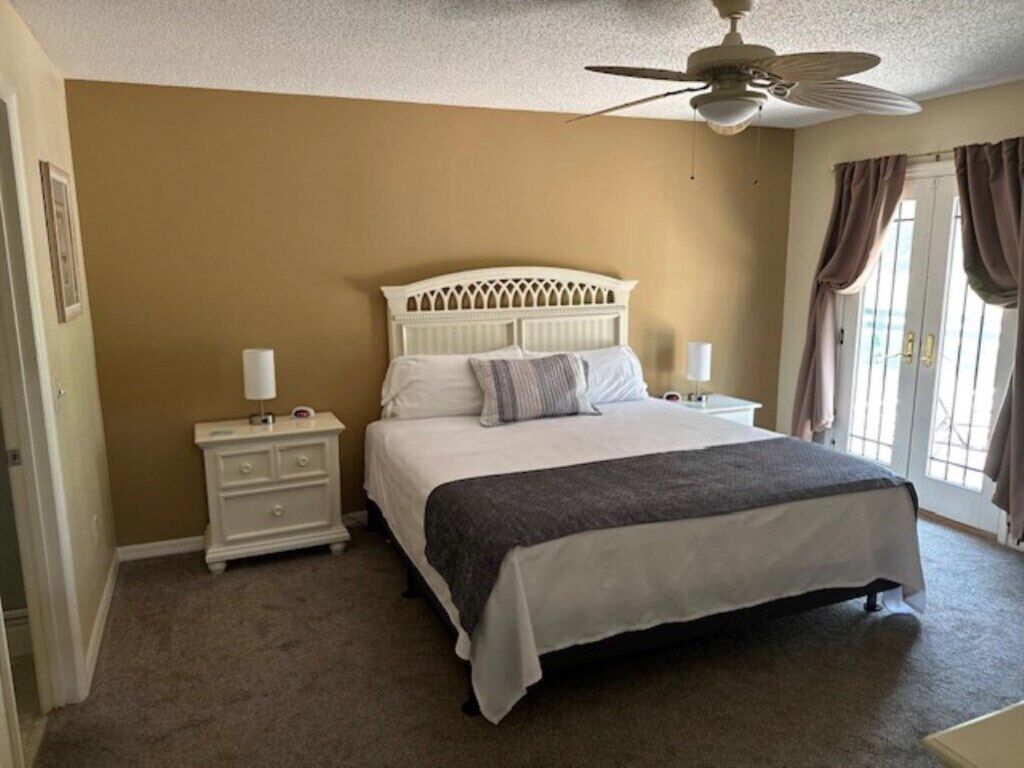 Une chambre à coucher avec un lit, des tables de chevet, un ventilateur de plafond et une fenêtre avec des rideaux.