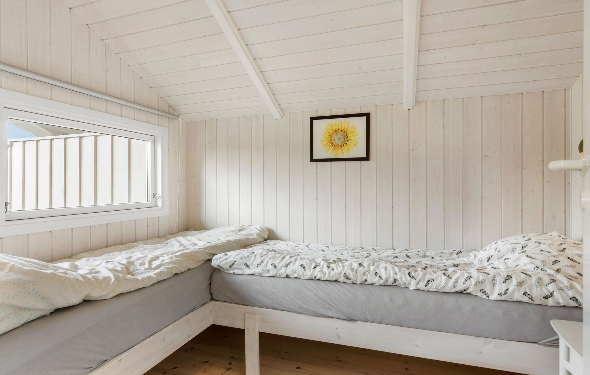 A room with a bed, a window, and a sunflower painting.