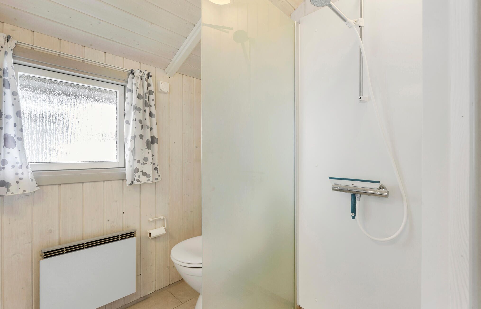 A bathroom with a toilet, a shower, and a window with curtains.