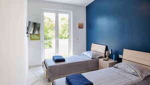 Een slaapkamer met twee bedden, een televisie aan de muur en een raam met uitzicht op groen.