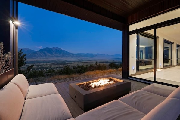 A modern outdoor seating area with a fire feature, overlooking a mountainous landscape.