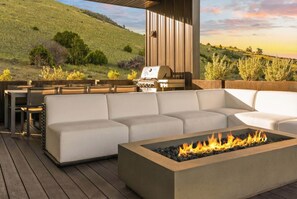 Une terrasse extérieure dotée d’un foyer, d’un barbecue et d’un espace salon avec un canapé et des fauteuils.