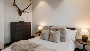 Una camera da letto con un letto grande, due comodini con lampade, una cassettiera in legno e una decorazione a corna di cervo appesa al muro.