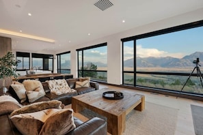 A modern living room with a large window offering a mountain view, a wooden coffee table, and a leather sofa with decorative pillows.