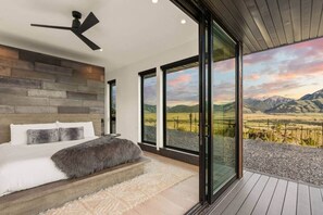 Une chambre moderne avec un grand lit, un ventilateur de plafond et une vue sur un paysage montagneux, visible à travers de grandes portes coulissantes.