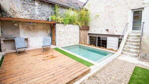A pool area with a wooden deck, two lounge chairs, a stone wall, and a small staircase. - Maison paradisiaque avec piscine (Mosnes)