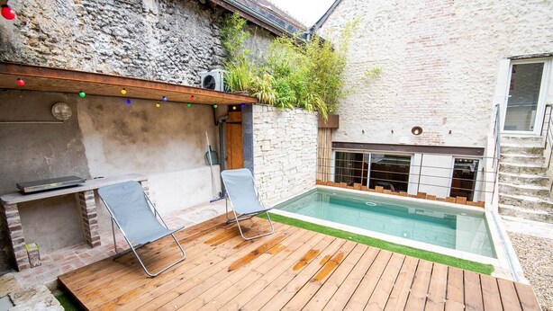 A poolside area with a wooden deck, two lounge chairs, a small pool, and a stone wall with greenery. - Maison paradisiaque avec piscine (Mosnes)