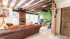 A cozy living room with a brown sofa, a fireplace, and a staircase leading to an upper level. - Maison paradisiaque avec piscine (Mosnes)