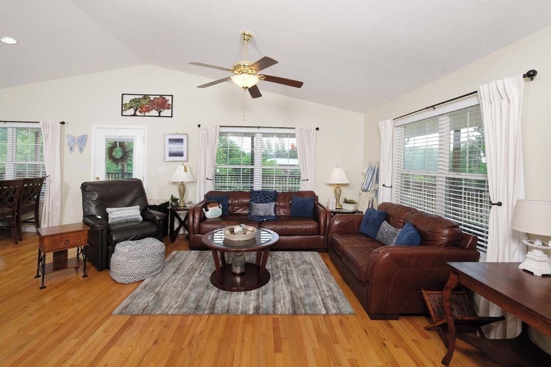 A spacious living room with a ceiling fan, leather sofas, a coffee table, and a dining area with a wooden table and chairs.