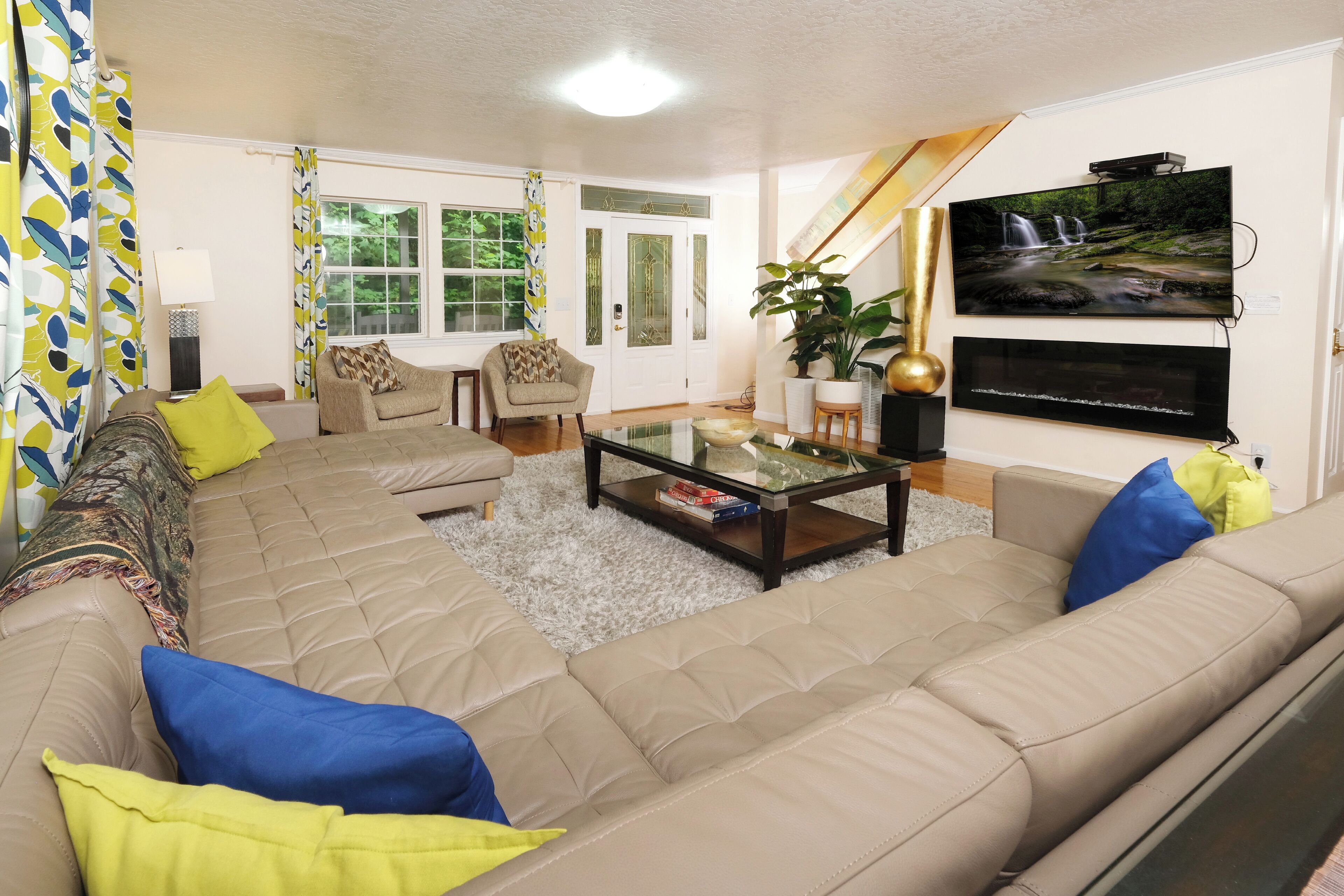 A living room with a beige sectional sofa, a glass coffee table, and a flat-screen TV mounted on the wall.