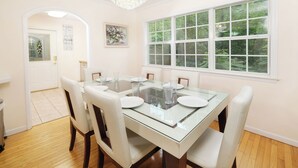 A dining area with a glass-top table, white chairs, a chandelier, a window with a view of trees, and a door with a sign. - Hop, Skip and a Jump: Minutes from the Mountains (Sevierville)