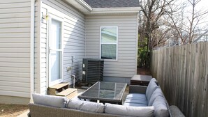A patio area with wicker furniture, a glass table, and a window. - Pet Friendly Water View Cottage (Pasadena)